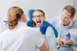Child smiling comfortably during first dental visit with friendly dentist and parent nearby